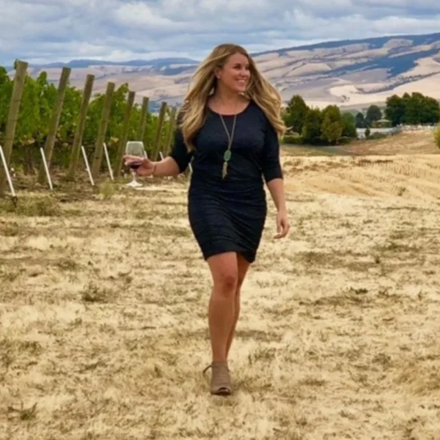 Travel Advisor Lindsay Marra with a blue dress and holding a wine glass with vineyards around.