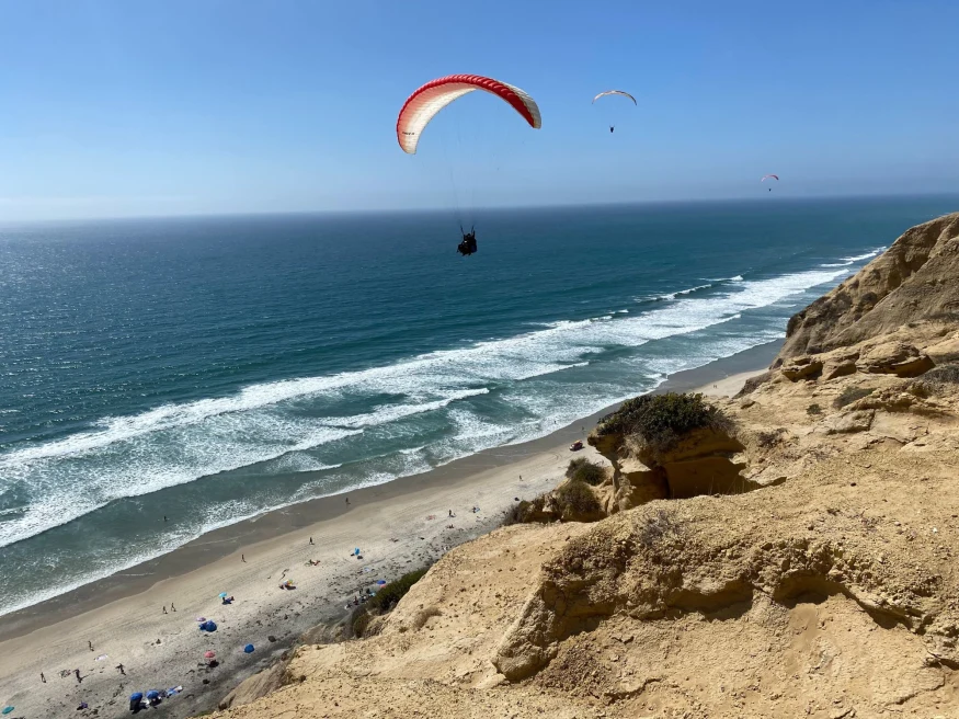 hang glider with a red sail over the coast with bright blue sky