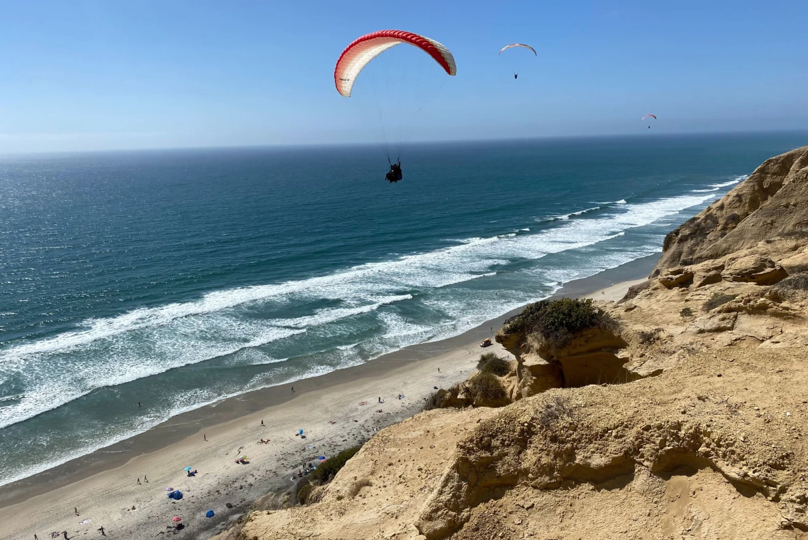 hang glider with a red sail over the coast with bright blue sky