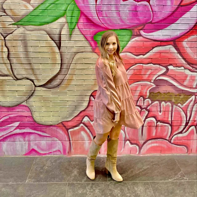 Picture of Morgan in a pink dress standing in front a colorfully floral mural
