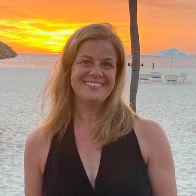 Travel advisor Lisa Dahling-Thompson on a beach during sunset wearing a black top.