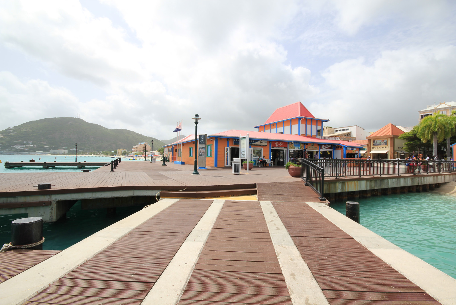 A brown and white pier with crystal blue waters and an orange roofed building in Saint Martin.