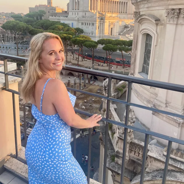 Courtney Head in a blue dress posing in front of a balcony.