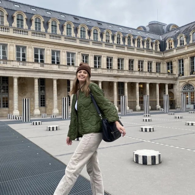 Travel Advisor Savannah Baker wears black covers and a army green coat in a Parisian courtyard. 