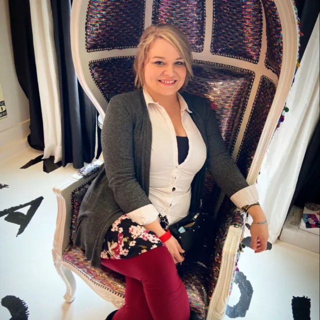 Travel Advisor Brittney Leigh sitting in a purple and white chair wearing a white shirt, grey cardigan and red leggings with a floral skirt.