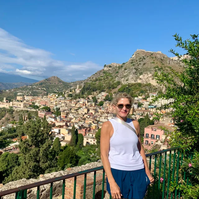 Picture of Kathleen wearing a white top with a view of the city, mountains and green trees in the background