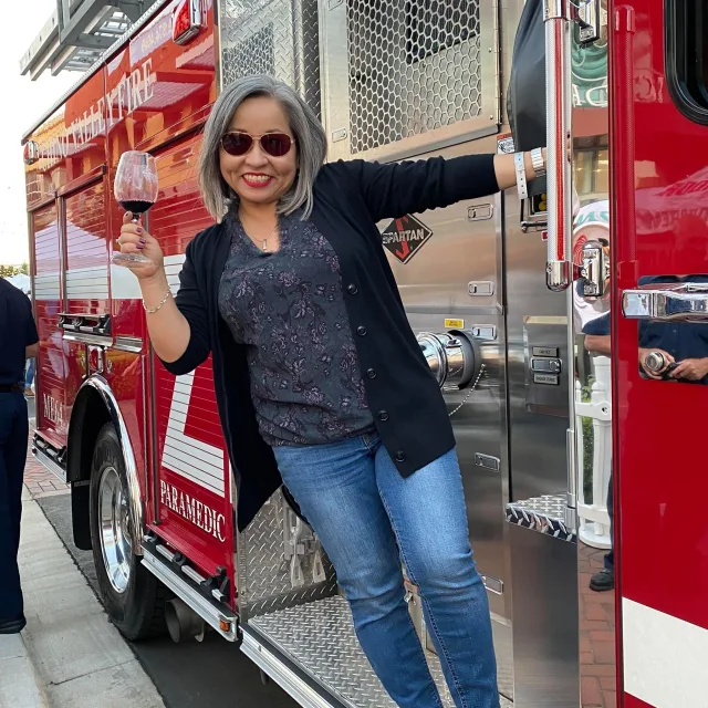 travel advisor Susie Pinedo holds a glass and wine and leans out of an ambulance