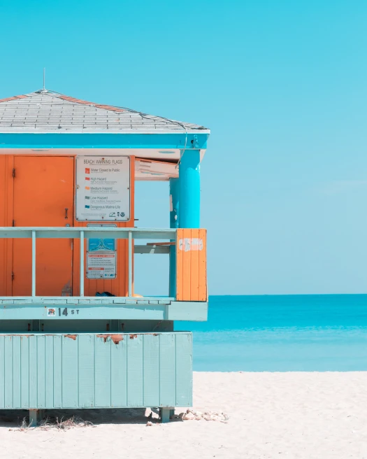Lifeguard post in South Beach painted bright blue and orange on sandy shore.