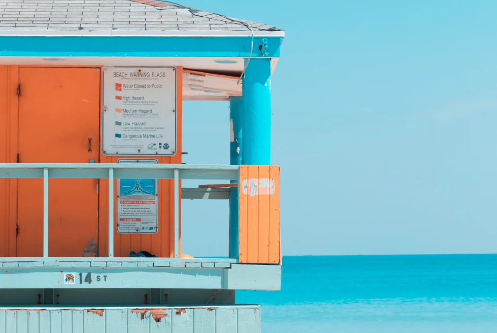 Lifeguard post in South Beach painted bright blue and orange on sandy shore.