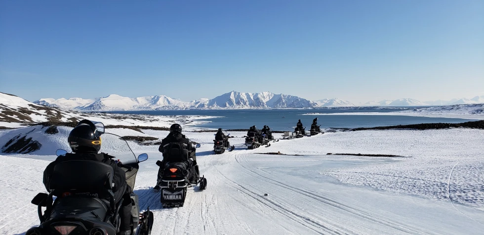 People wearing black jackets riding on snowmobiles across snowy landscape during daytime