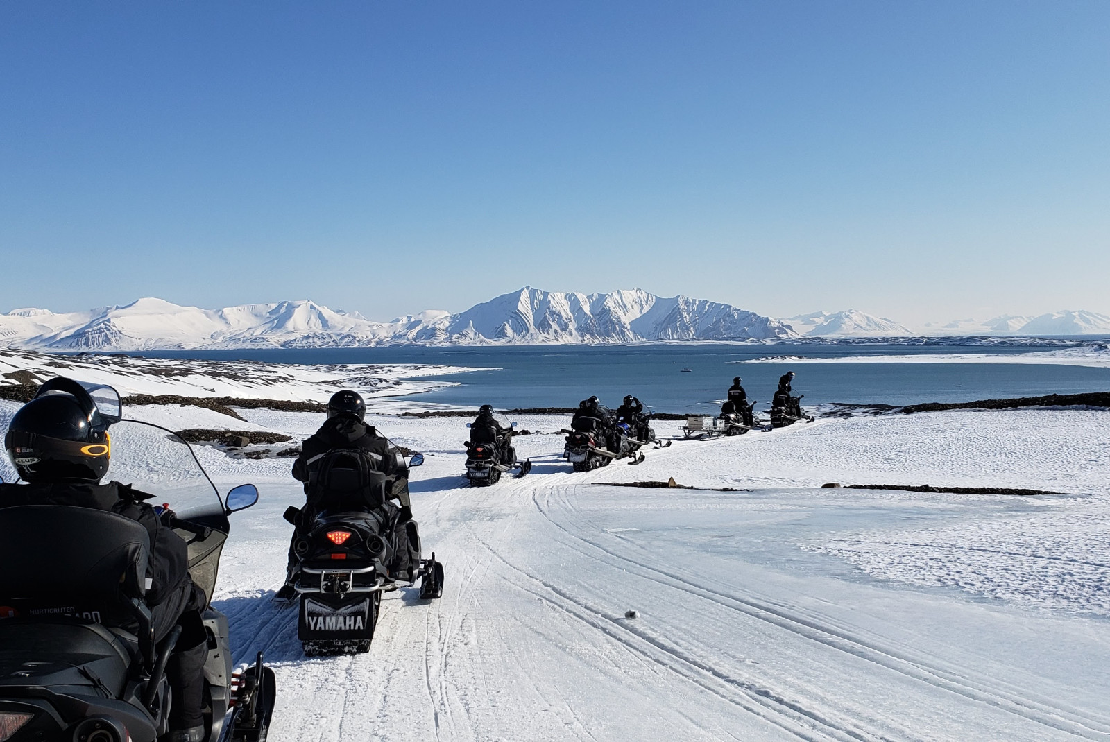 People wearing black jackets riding on snowmobiles across snowy landscape during daytime
