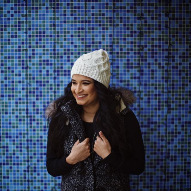 Seema Desai Travel Agent wearing white hat and black jacket standing in front of blue tiled wall