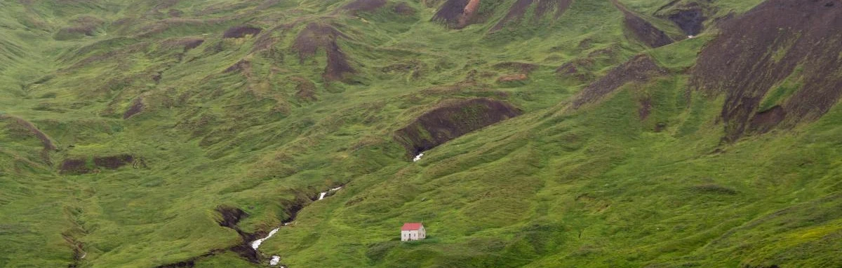 Mysterious house on green mountain pastures next to the ocean on a foggy day in Iceland.