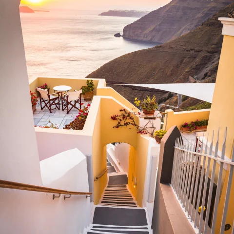 A white-washed staircase flanked by buildings in front of the Mediterranean in Greece. 