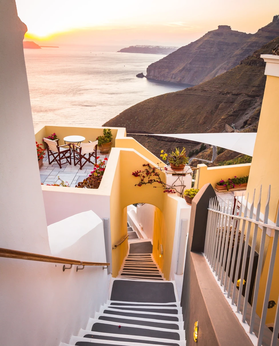 A white-washed staircase flanked by buildings in front of the Mediterranean in Greece. 