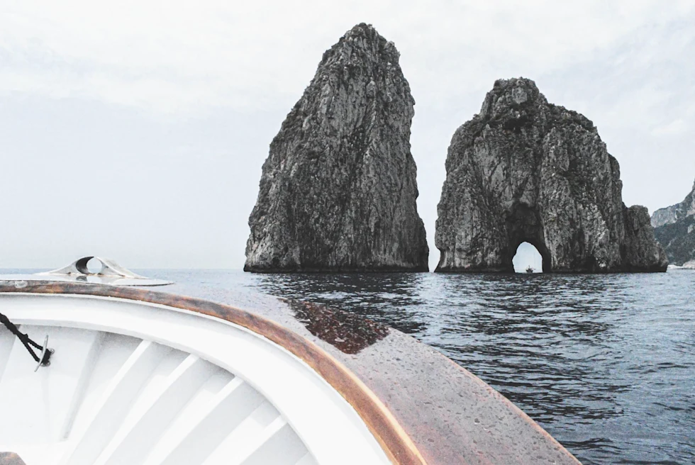 rock formation in the water ahead of the bow of a white wooden boat