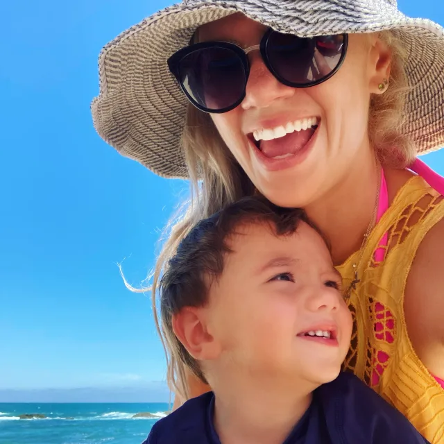 Travel Advisor Sarah Sukta in sunglasses and a hat with kid on a beach. 