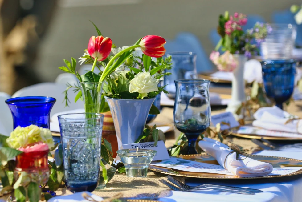 Long table set with red and yellow flowers in vases and blue glasses and gold plates
