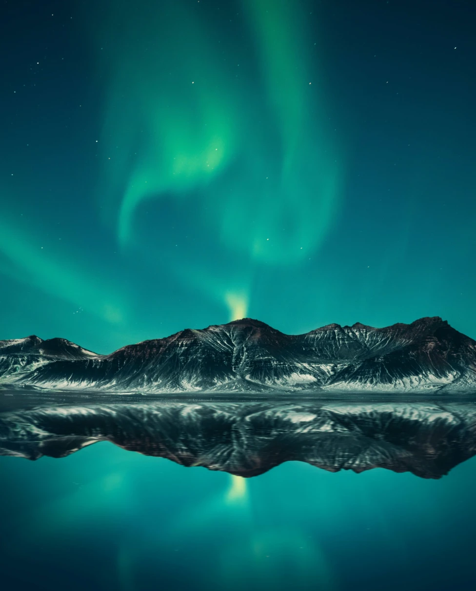 A picture of green aurora lights in the sky at night over hills on a body of water.