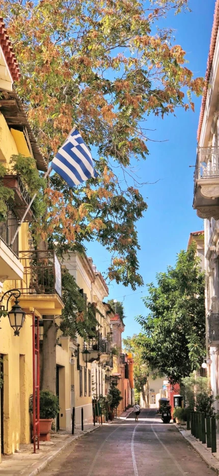 Sunny Athens backstreet with colorful townhouses, one of which is waving the Greek flag. 