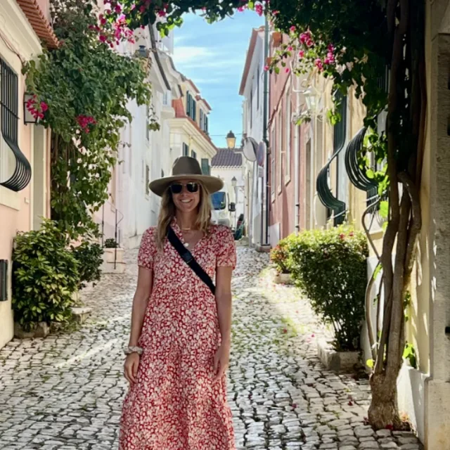 Travel Advisor Gianna Quattrini in a red and white sun dress and hat standing in a cobblestoned alleyway.