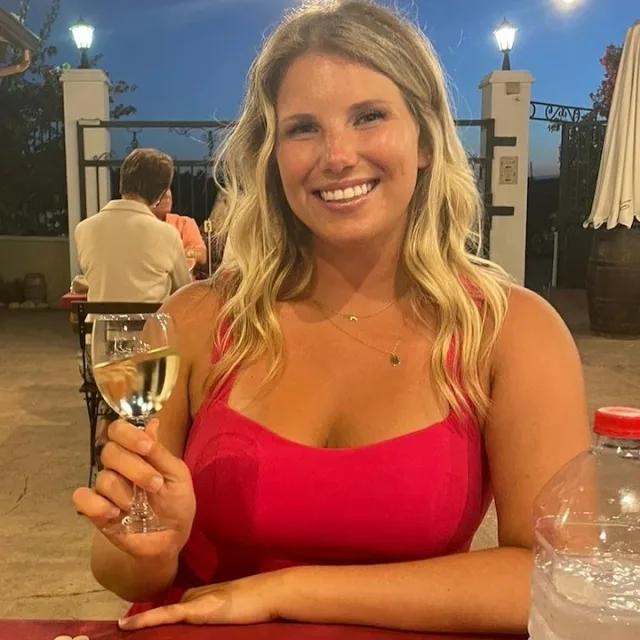 Picture of Maddie in red dress with a wine glass in hand in a restaurant. 