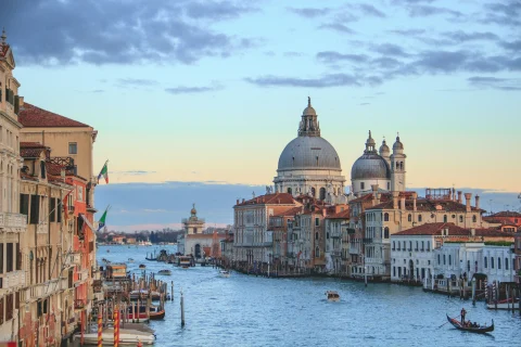 A landscape view of Venice, with St. Mark's Basilica, buildings, and gondolas in the canal right before sunset.