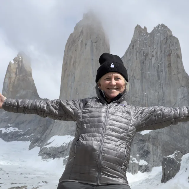 Travel Advisor Nicole Buie in a silver puffer jacket and black hat in front of snow capped mountains.