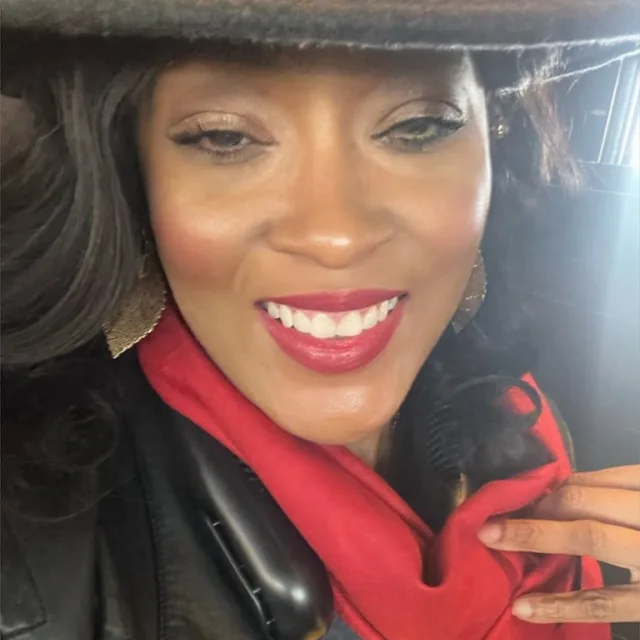 Travel Advisor Kendra Hearn, Ph.D. in a black hat and red scarf with gold earrings.