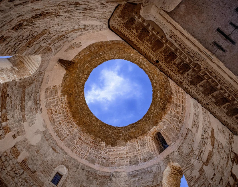 looking up at a perfect circular skylight opening revealing bright blue sky in an ancient stone building  