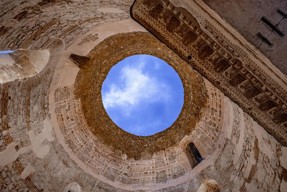 looking up at a perfect circular skylight opening revealing bright blue sky in an ancient stone building