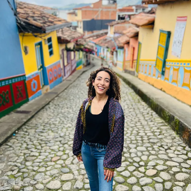 Travel Advisor Sara Tohamy in jeans and a purple shirt in front of colorful houses on a cobblestone street.