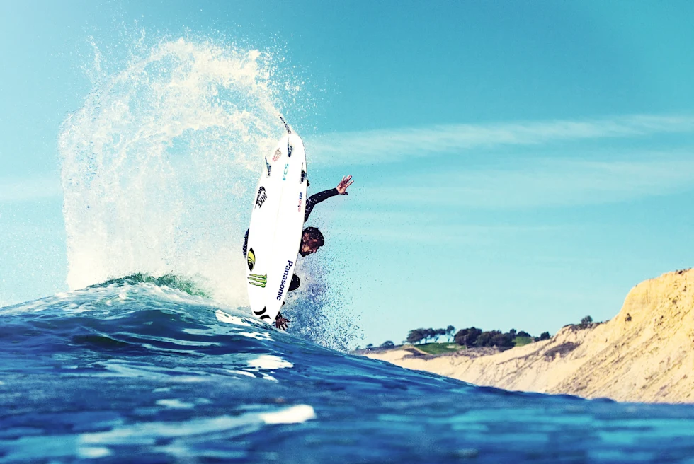 A surfer in Morocco splashing white and blue water while doing a trick on a wave with a tan cliff in the background.