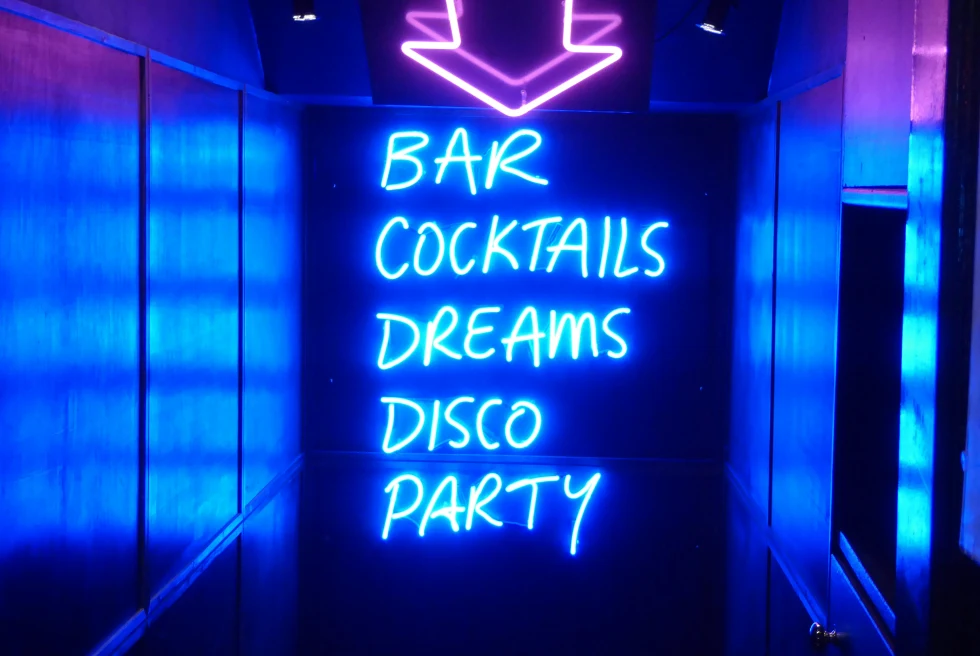 A lit up sign to a bar that says "BAR COCKTAILS DREAMS DISCO PARTY"
