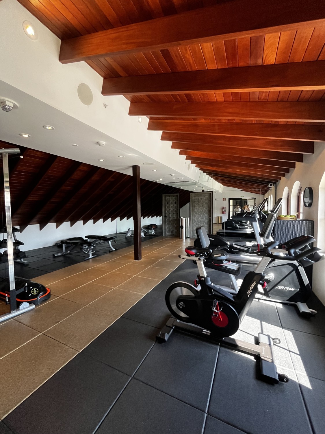 A workout facility with a wood paneled ceiling, black mat flooring and white walls. 