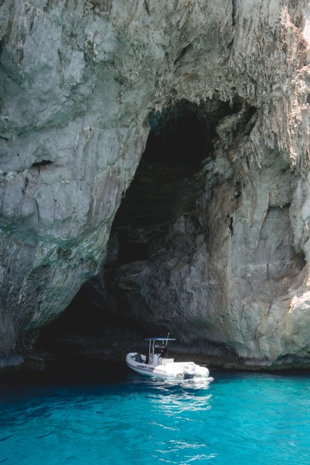White boat sits in blue waters near a grotto in Italy