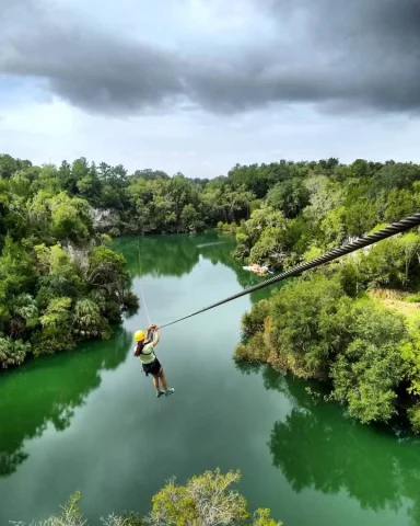 A person ziplining over a body of water surrounded by trees