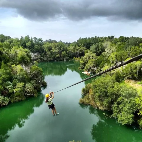 A person ziplining over a body of water surrounded by trees