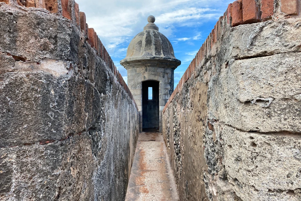path in between two stone walls leading to a bell tower