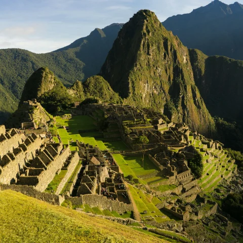 An aerial view of Machu Picchu, Peru complete with lush green grass and mountain ranges in the distance. 