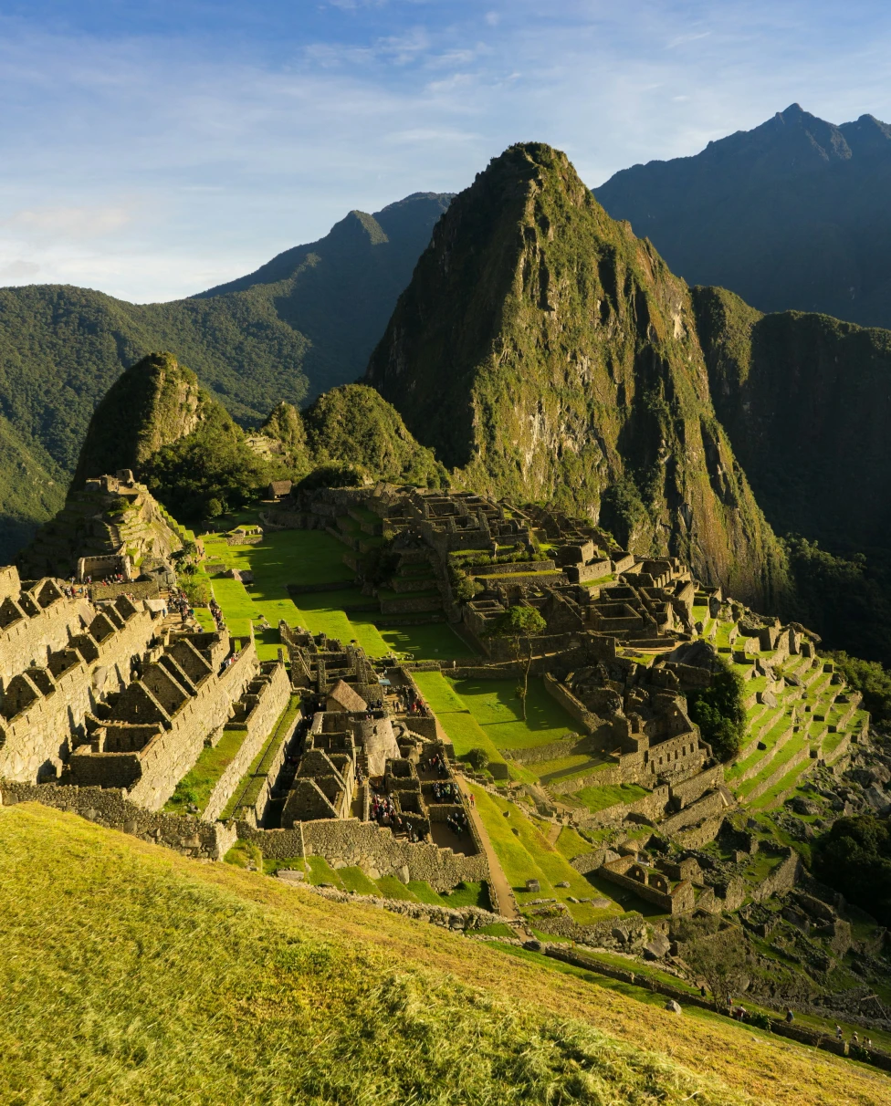 An aerial view of Machu Picchu, Peru complete with lush green grass and mountain ranges in the distance. 