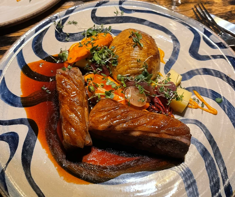 A piece of meat and potatoes on a swirly-blue dish. 