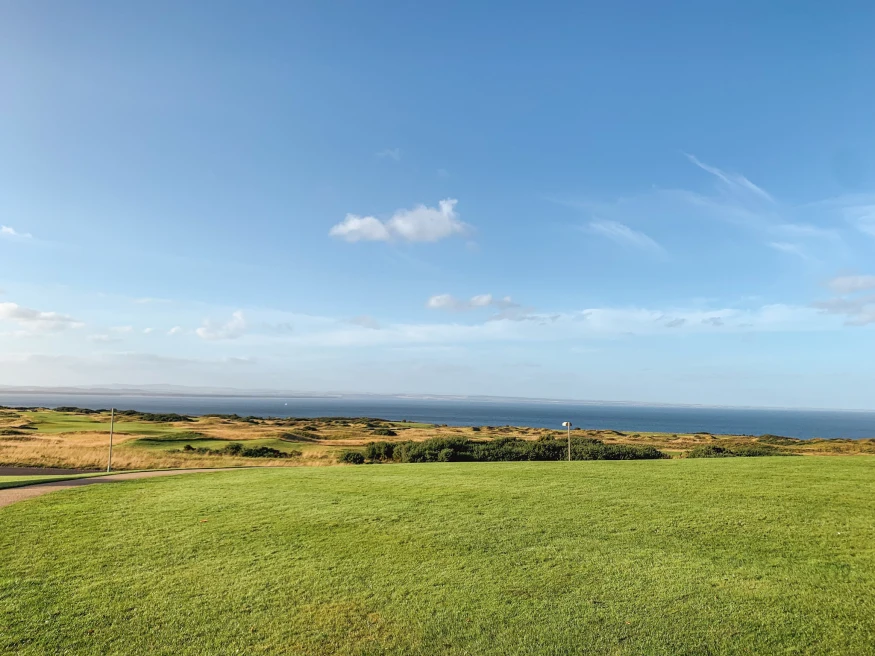 green and tan grass golf course with ocean in the distance and blue sky 