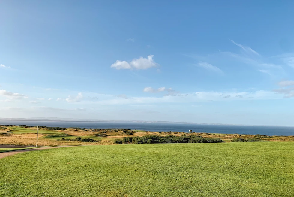 green and tan grass golf course with ocean in the distance and blue sky