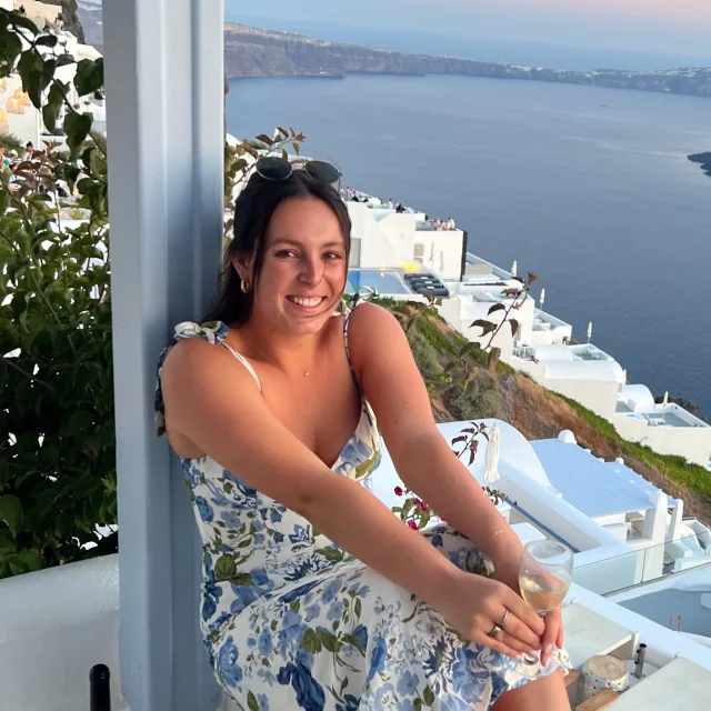  Travel Advisor Megan Daly with a floral dress and white houses overlooking the sea.