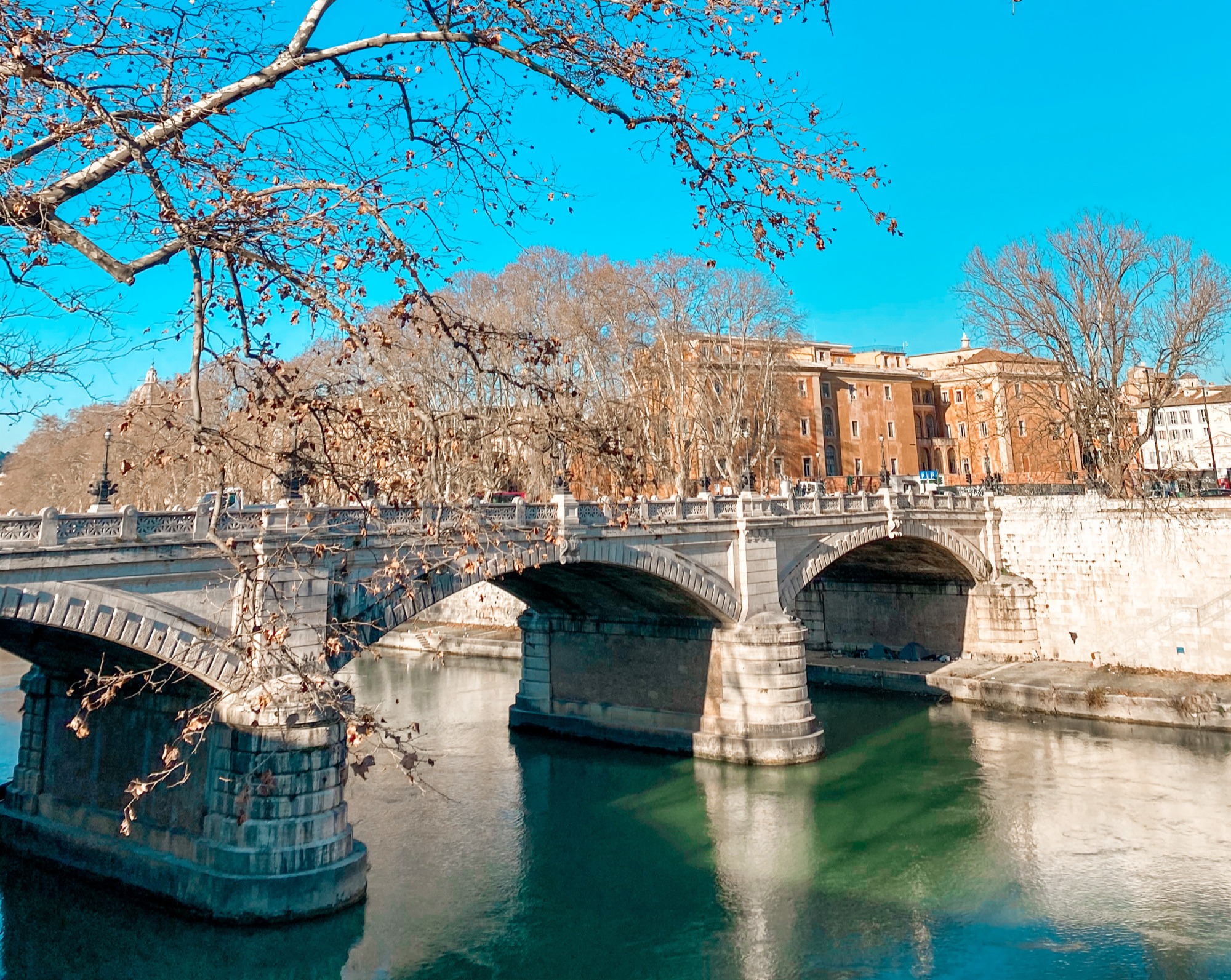stone bridge with 3 arches over river with clear blue sky 