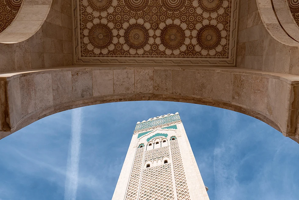 White and blue Mosque in Casablanka with blue sky under a stone arch