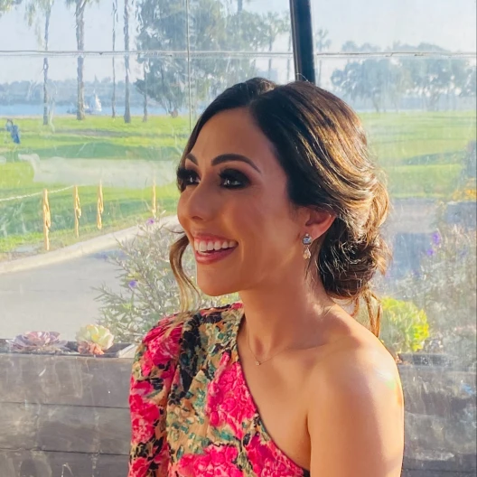 Travel Advisor Diana Popal in a pink floral dress with trees and water in the background.