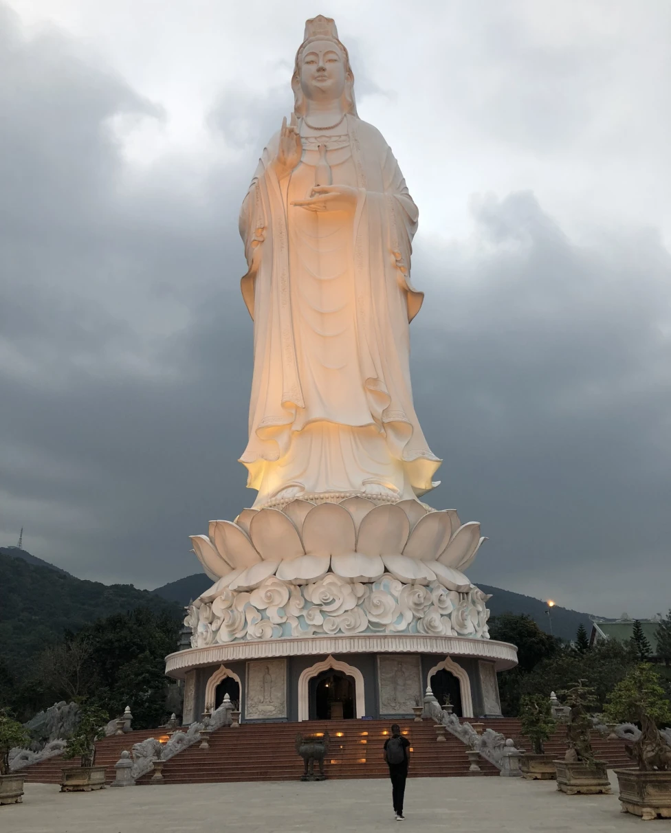 A low-angled shot of a Lady Buddha statue made out of a white stone and lit up at daytime. 