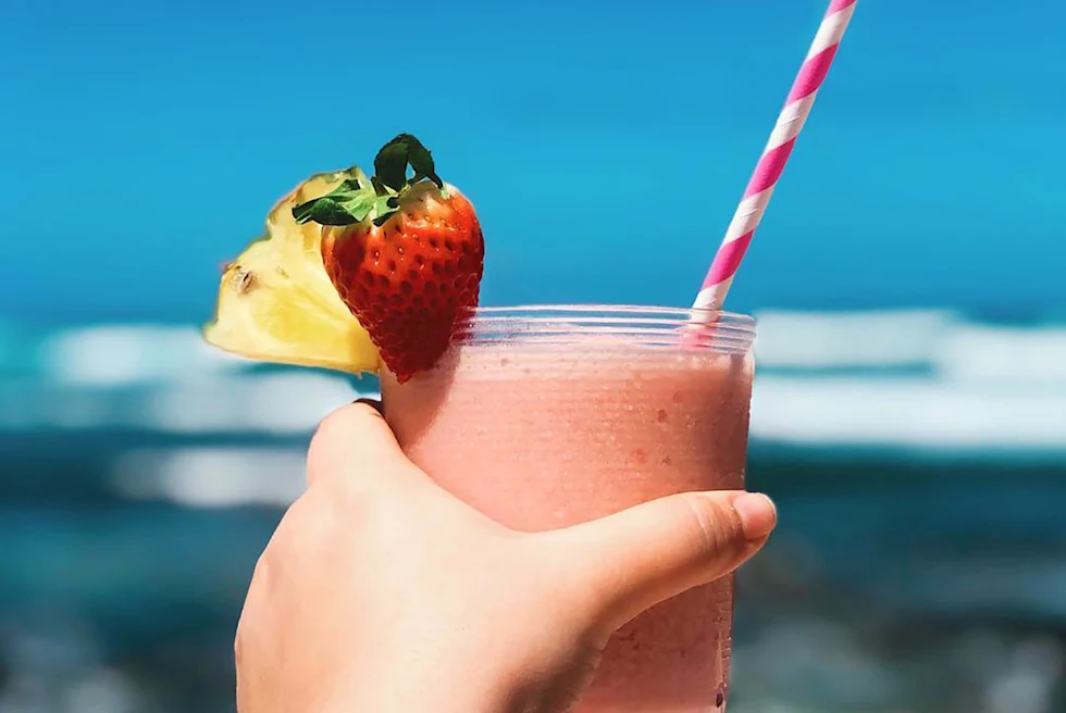 hand holding pink smooth with strawberry pineapple and a pink and white striped straw